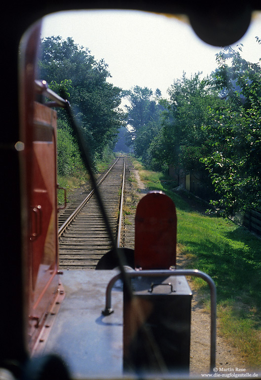 In den Anfangsjahren meiner Eisenbahnfotografie hatte ich nur selten die Möglichkeit zur Mitfahrt im Führerraum. Entsprechend wenige Fotos finden sich in meinem Archiv. Auf Anfrage nahm mich am 2.7.1986 das Lokpersonal der 323 176 mit auf der 8 Kilometer langen Kleinbahn Lohne – Dinklage. Dabei machte ich auch ein Foto aus dem Führerstandsfenster auf die Strecke.